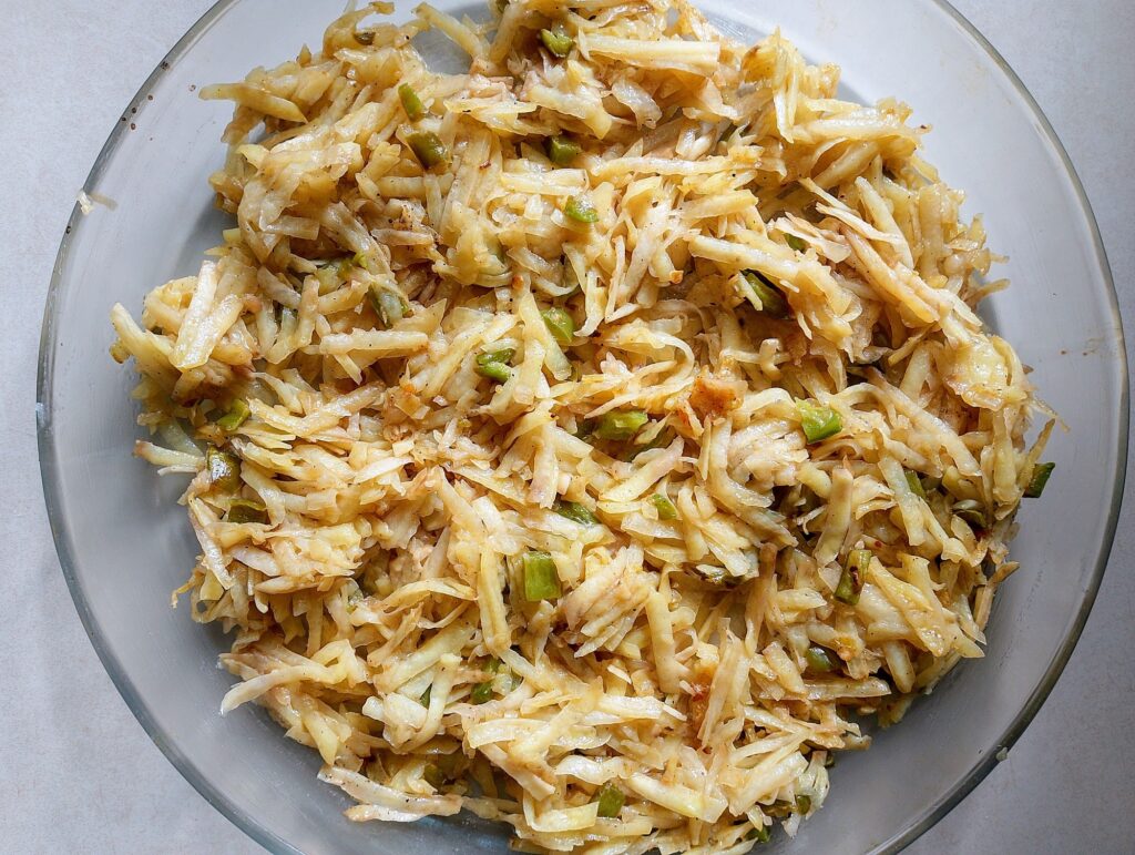Filling the greased baking dish with the sauteed bell pepper and shredded potatoes