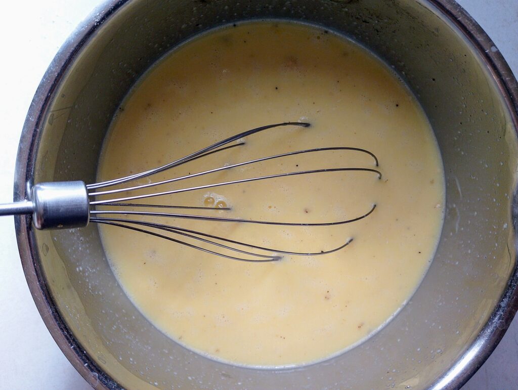 Whisking together eggs, milk, onion powder, salt, and pepper to make the Amish casserole filling
