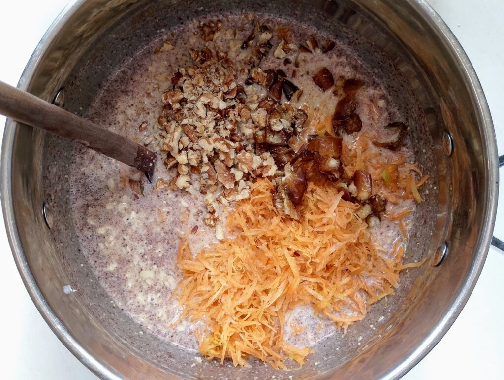 Stirring grated carrots, chopped walnuts, and dates to the rest of the ingredients for the baked oatmeal in the mixing bowl