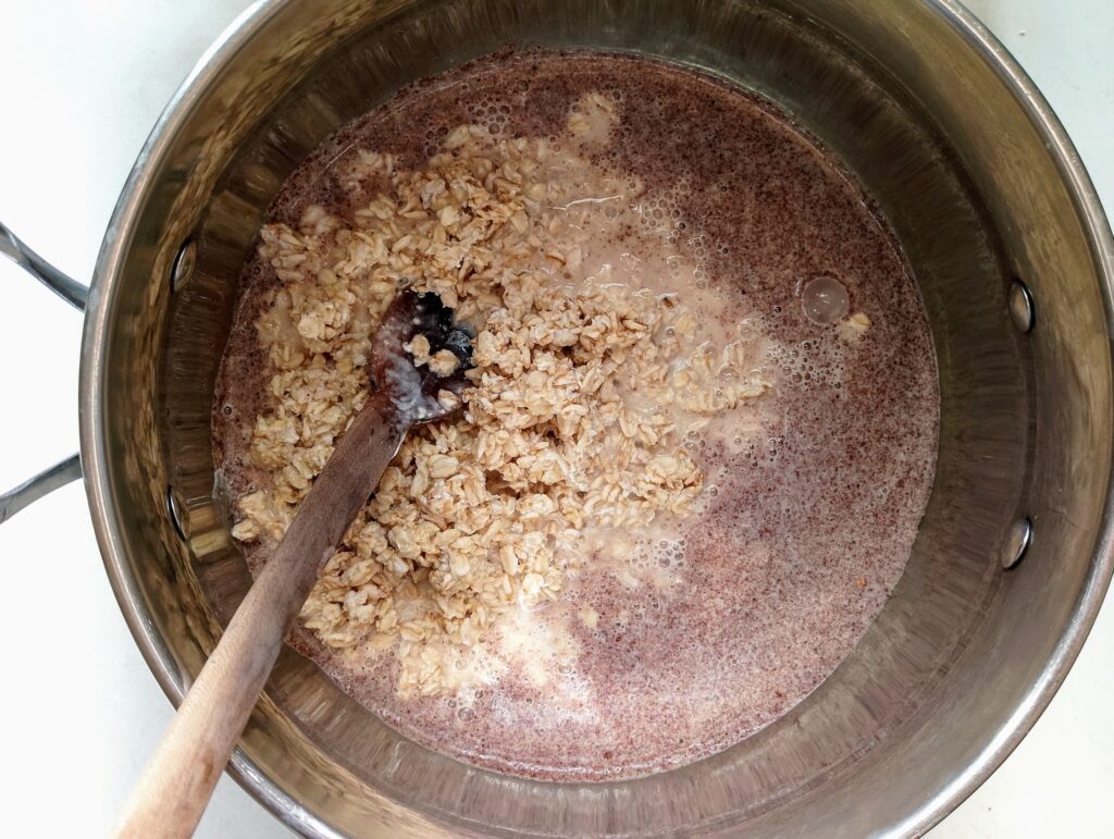 Adding soaked and drained oatmeal to the wet ingredients for the baked oatmeal in th mixing bowl