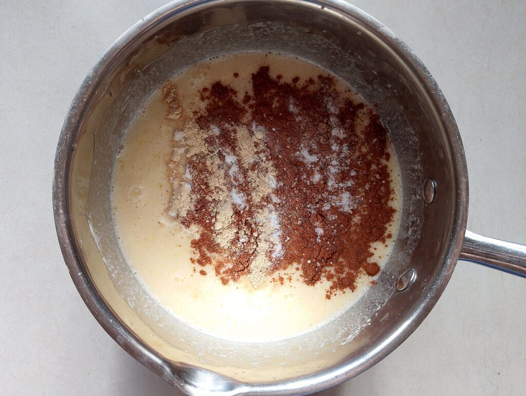 Adding cinnamon, ginger, cloves, baking soda, and salt to the custard mixture in the bowl