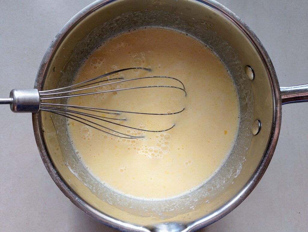 Whisking eggs, butter, cream, milk, and brown sugar in a mixing bowl