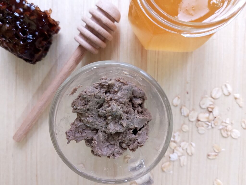Freshly prepared natural clay and oatmeal face mask with honey in a glass cup