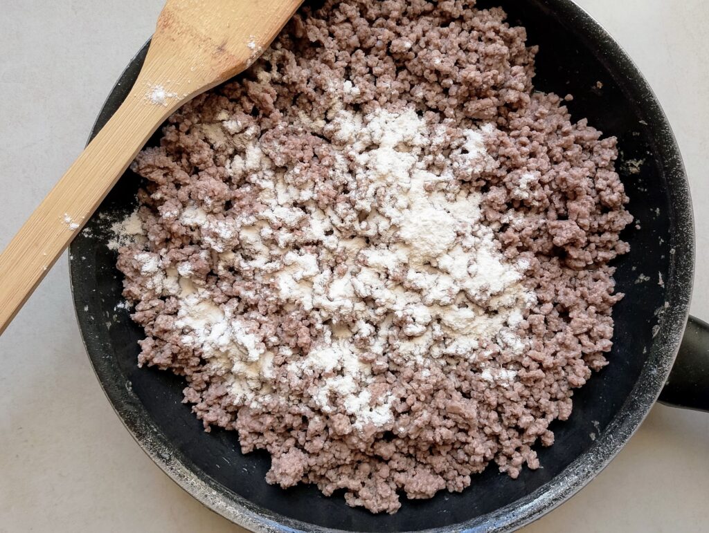 Adding flour to ground beef in the frying pan to create a thicker gravy