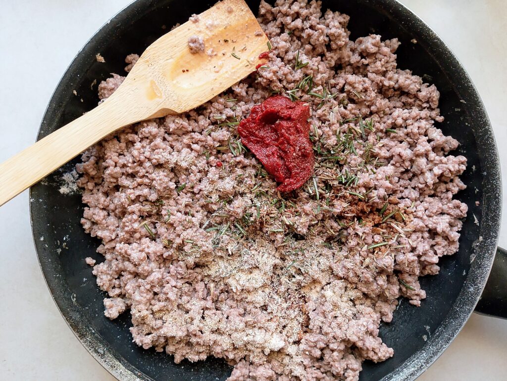 Adding tomato paste, vinegar, soy sauce, rosemary, thyme, garlic powder, and onion powder to the ground beef in the frying pan