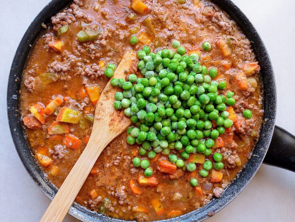 Adding green peas to the cottage pie filling in the pan