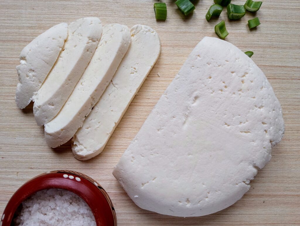 Sliced raw milk queso fresco wih some sliced green onions and a dish of coarse salt on the side