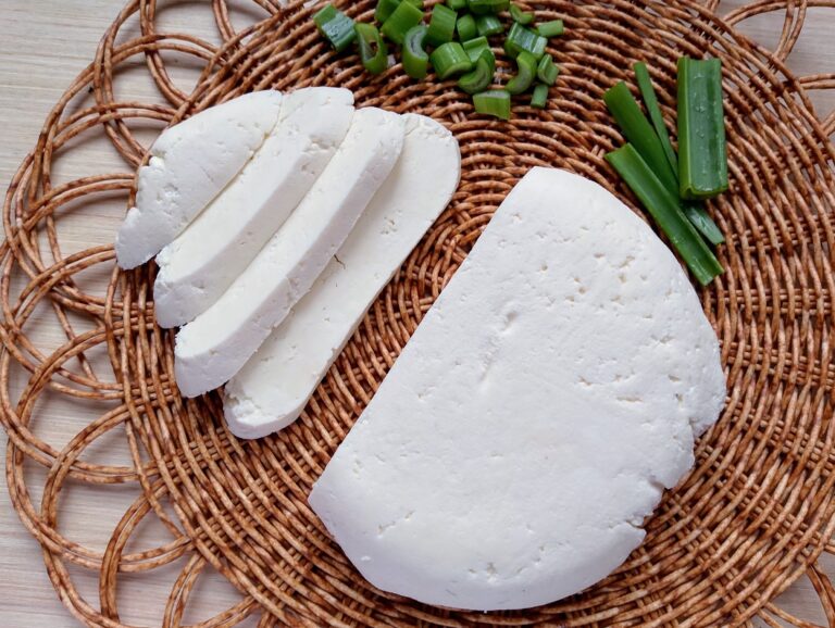 Raw milk queso fresco sliced on a wicker mat with sliced green onions on the side