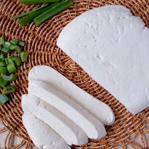 Raw milk queso fresco sliced on a wicker mat with some sliced green onions on the side