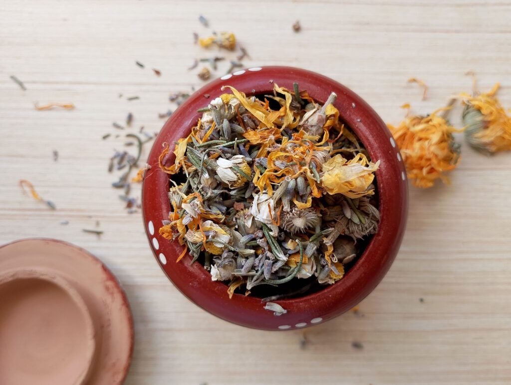 Small clay container filled with dried calendula, chamomile, lavender, and rosemary