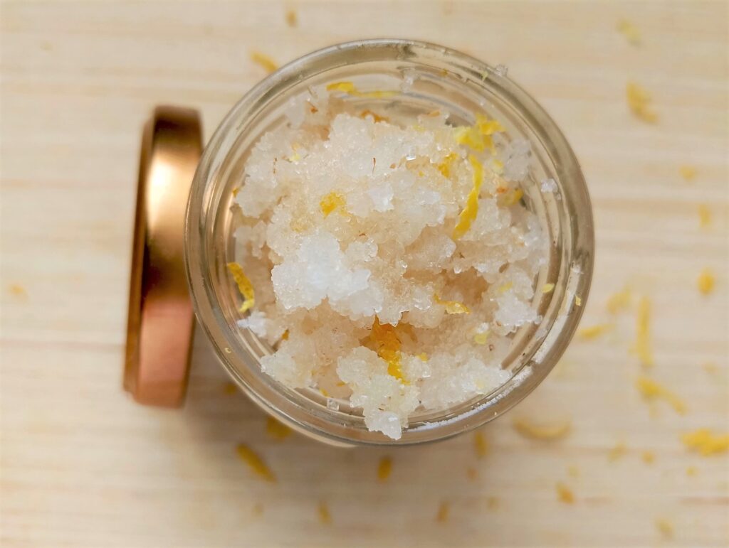 Filling a glass jar with the diy lemon and peppermint foot scrub for storage