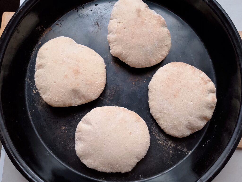 Freshly baked sourdough pita breads on an oven tray