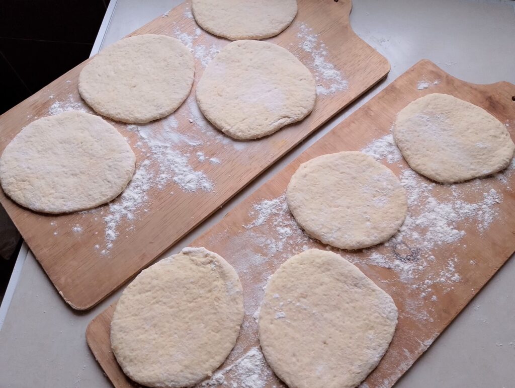 Rolled out pita breads on floured trays, resting before being baked