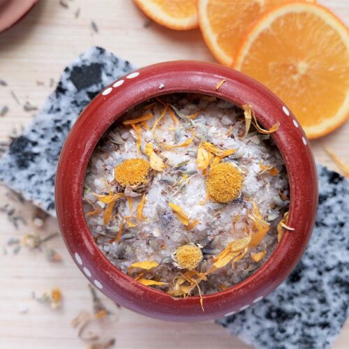 Homemade herbal bath salts in a small clay container with some dried calendula and lavender around