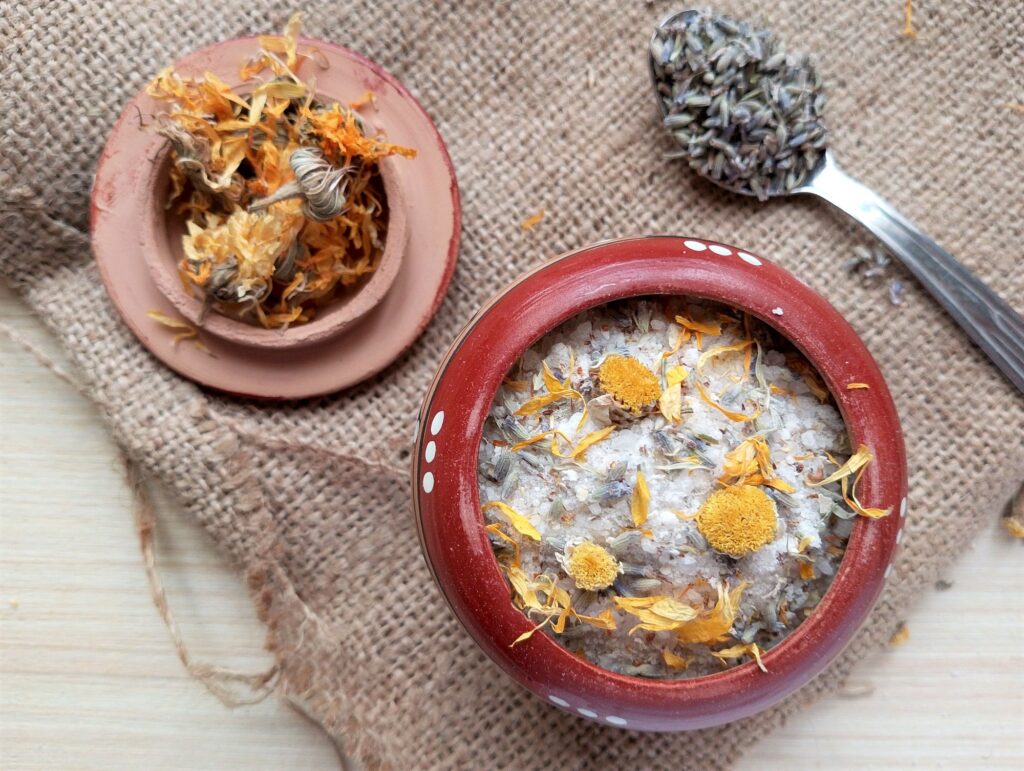 Homemade herbal bath salts in a small clay container with some calendula and lavender around 