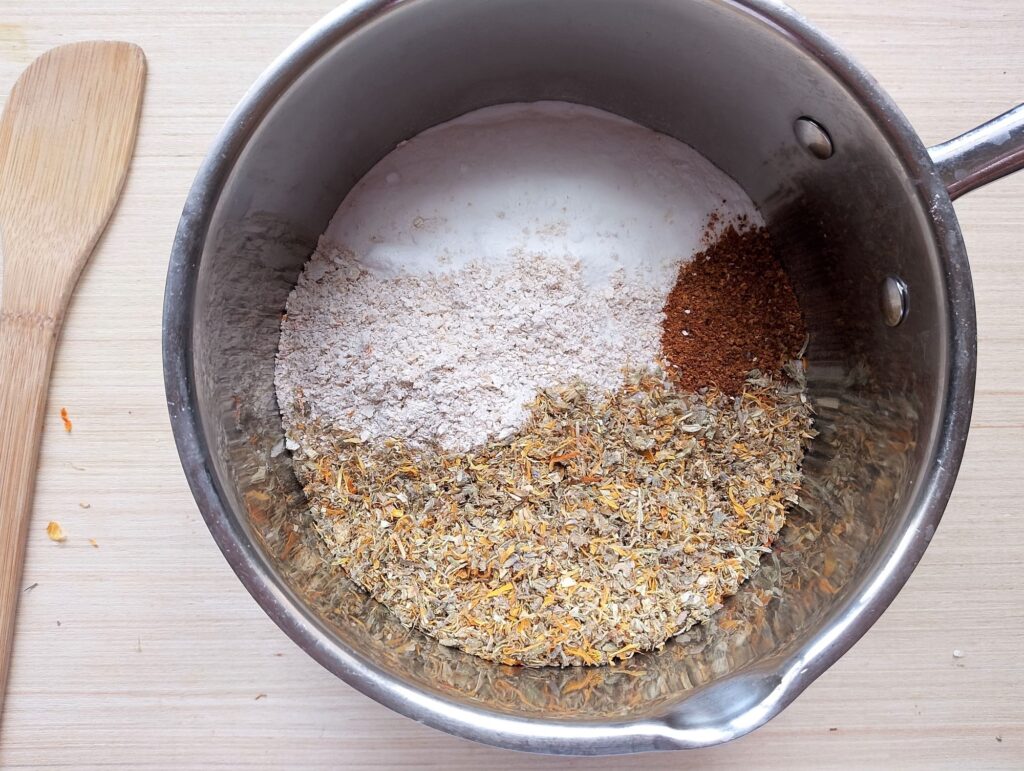 Mixing the crushed herbs, ground oats, and orange peel with salt and baking soda in a bowl