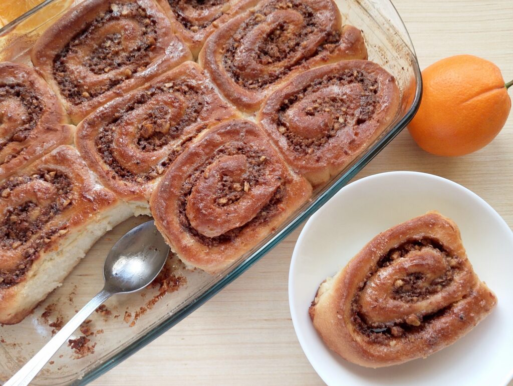 Sourdough discard orange cinnamon rolls in a baking dish with one roll removed onto a serving plate