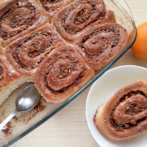 Sourdough discard orange cinnamon rolls in a baking dish with one roll removed onto a serving plate