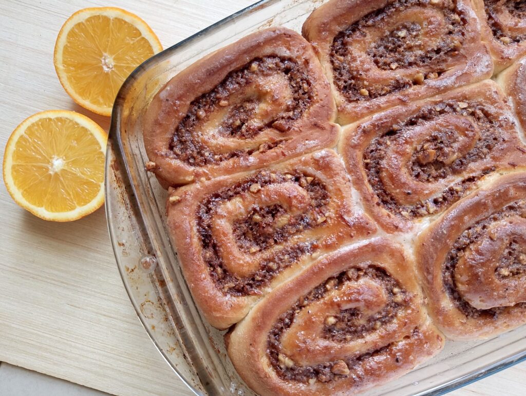 Freshly baked sourdough discard orange cinnamon rolls on a wooden tray with a halved orange on the side
