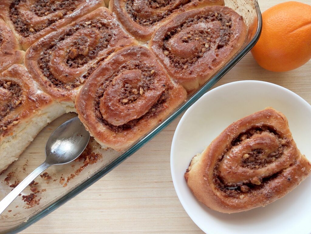 Sourdough discard orange cinnamon roll on a serving plate with the rest of the rolls still in the baking dish