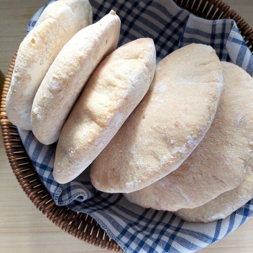 Sourdough pita breads in a basket lined with a tea towel