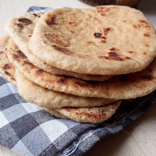 Sourdough whole wheat blend naan flatbreads stacked on a tea towel