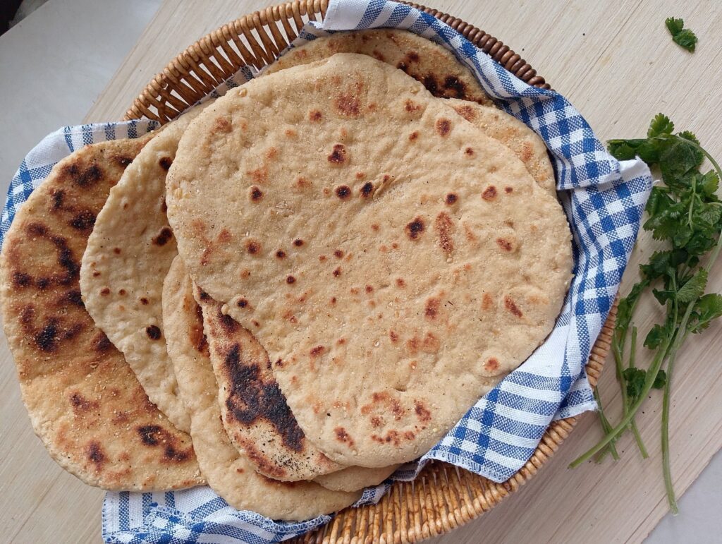 Sourdough whole wheat blend naan flatbreads stacked in a basket lined with a tea towel