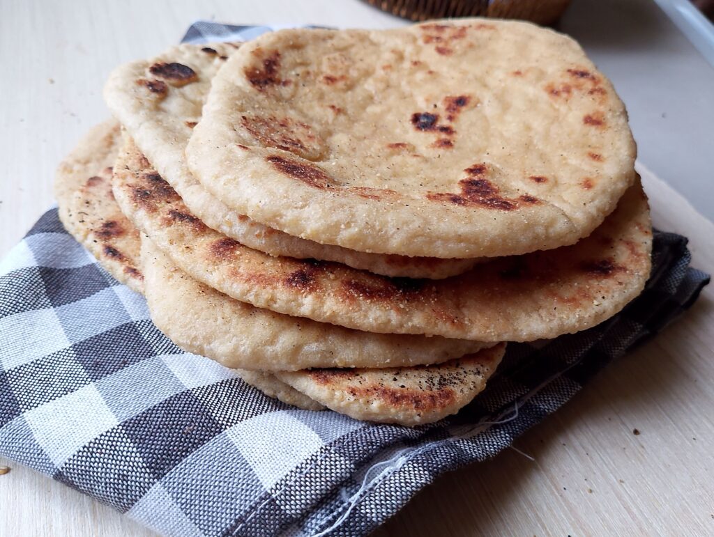 Freshly cooked sourdough naan flatbreads, stacked on a tea towel and ready to serve