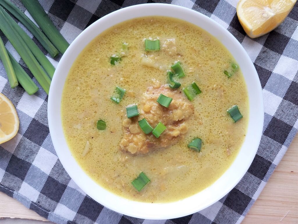 Red lentil and chicken stew served in a bowl with a garnish of sliced green onions