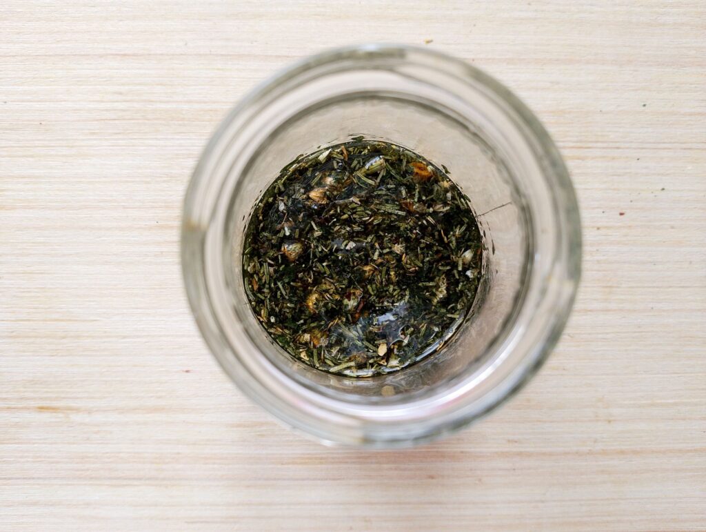 Pouring olive, jojoba and castor oils over the crushed herbs in the jar
