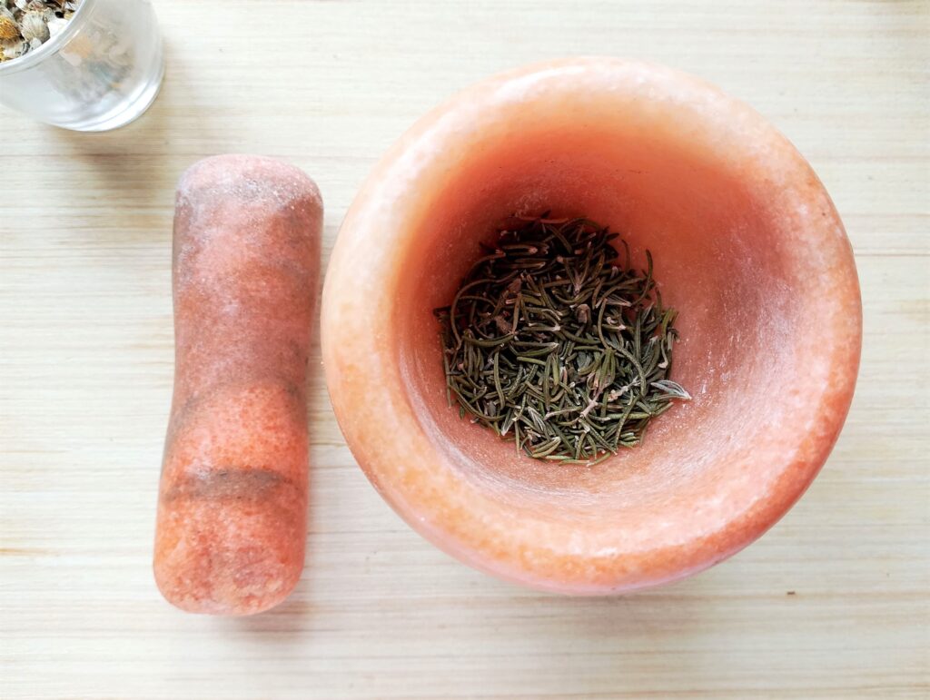 Crushing dried herbs in a pestle for the DIY hair and scalp oil