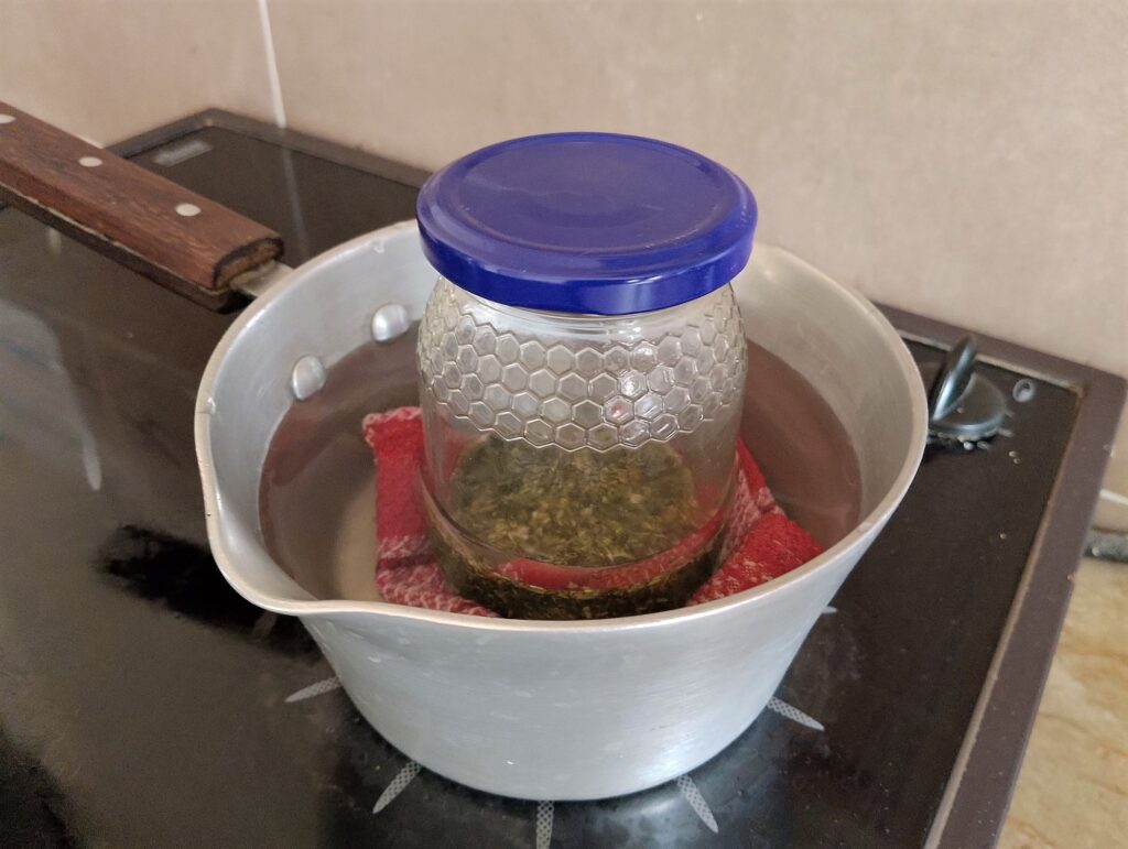 Infusing herbs in oil in a jar placed in a saucepan lined with a folded tea towel