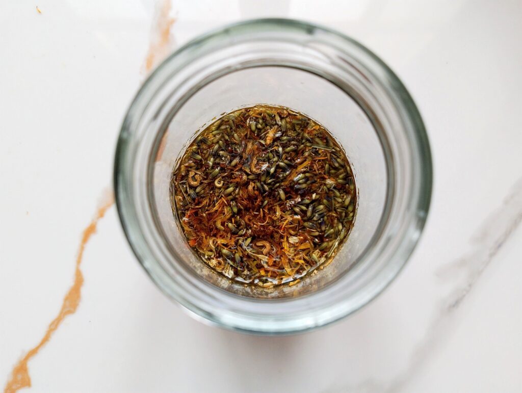 Adding the crushed herbs to the oils in a jar