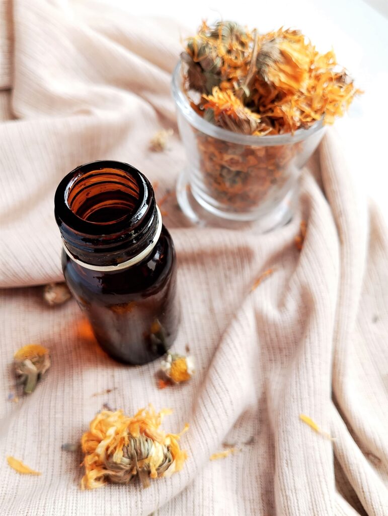 DIY herbal body oil in a dark amber bottle with a small cup of calendula on the side