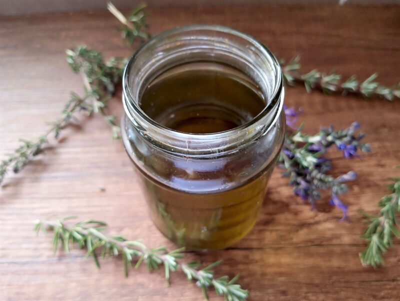 Rosemary infused oil in a jar with some rosemary sprigs scattered around it