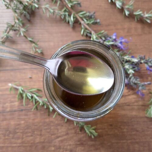 How to make herbal infused oils: a teaspoon lifting some rosemary infused oil out of a jar