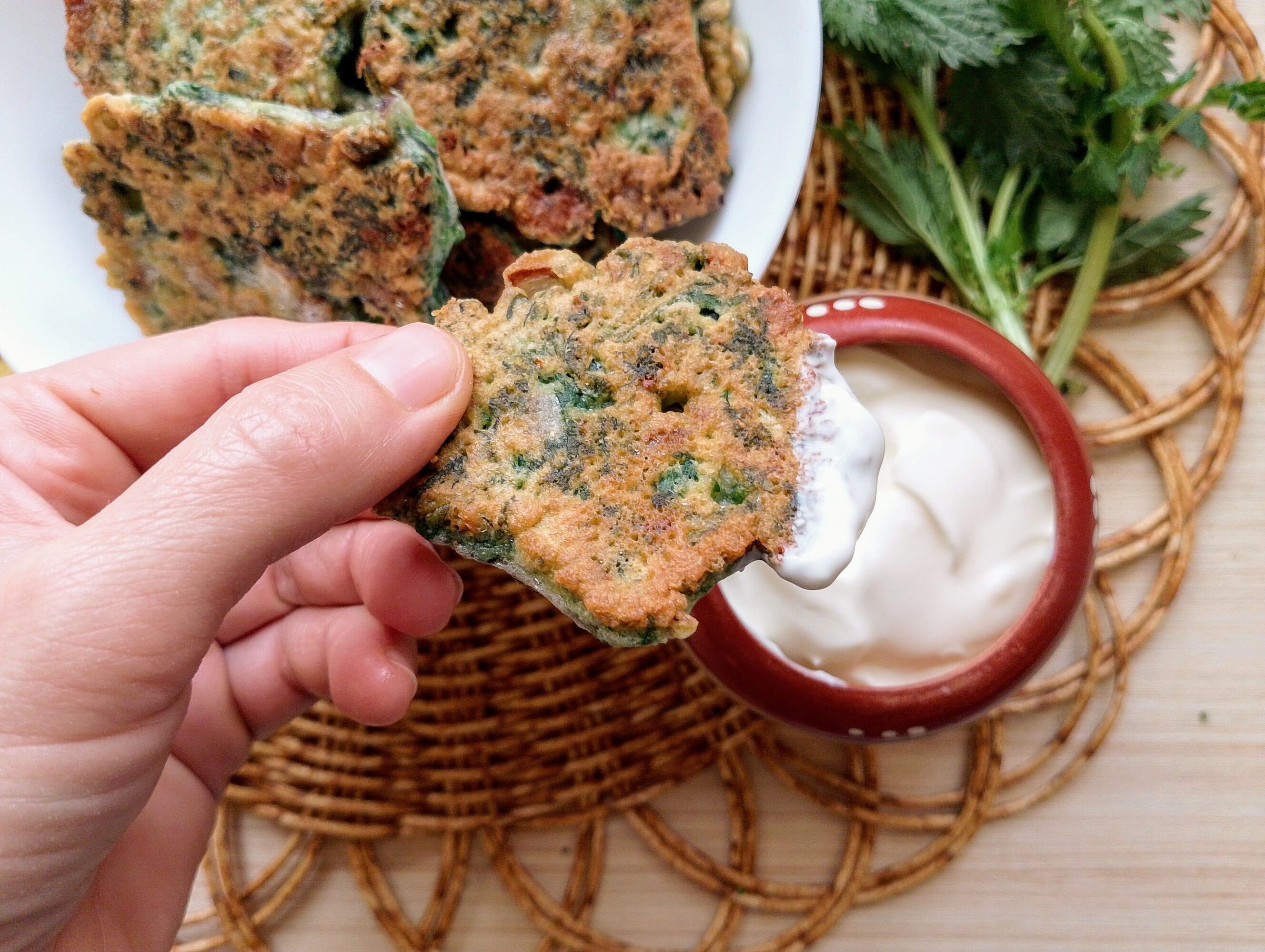 How to make nettle fritters: hand lifting a golden fritter with sour cream