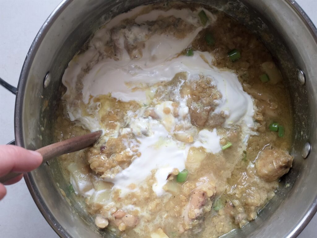 Stirring cream into the red lentil and chicken stew