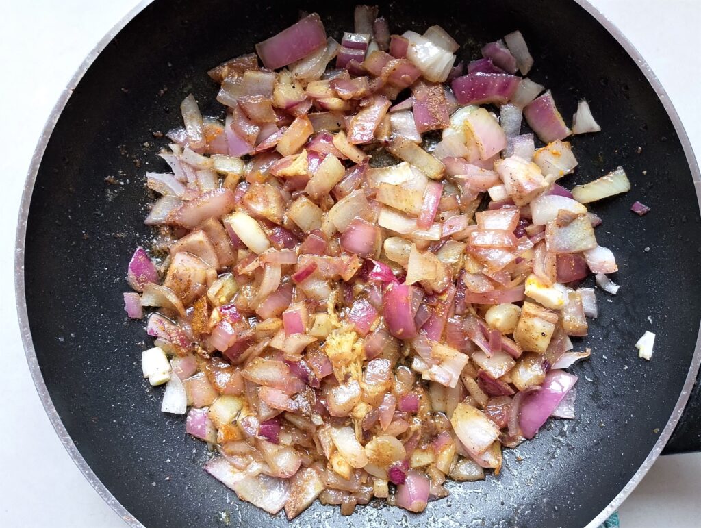 Stirring fresh garlic, fresh ginger, and spices into the chopped onion in the skillet