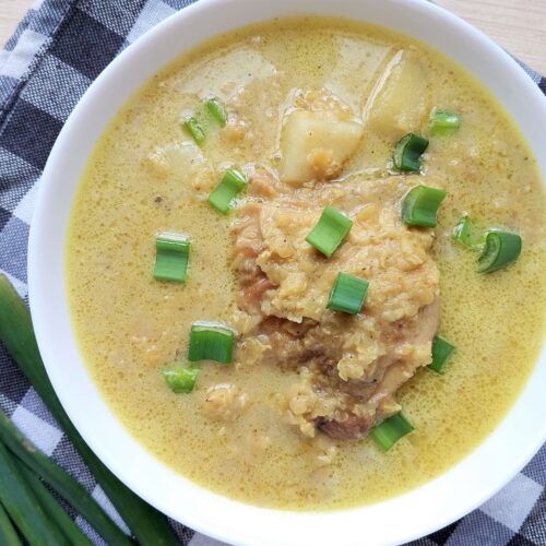 Red lentil and chicken stew served in a white bowl and garnished with sliced green onions