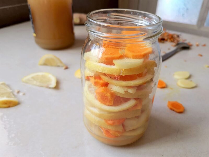 Sliced lemon, ginger, and turmeric layered in a jar, ready for fermenting in honey