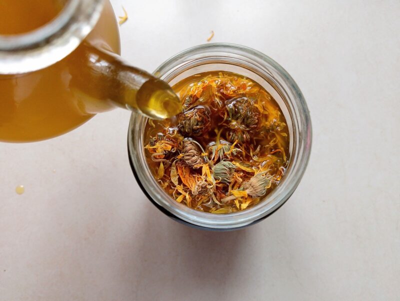 Pouring oil over dried calendula flowers in jar