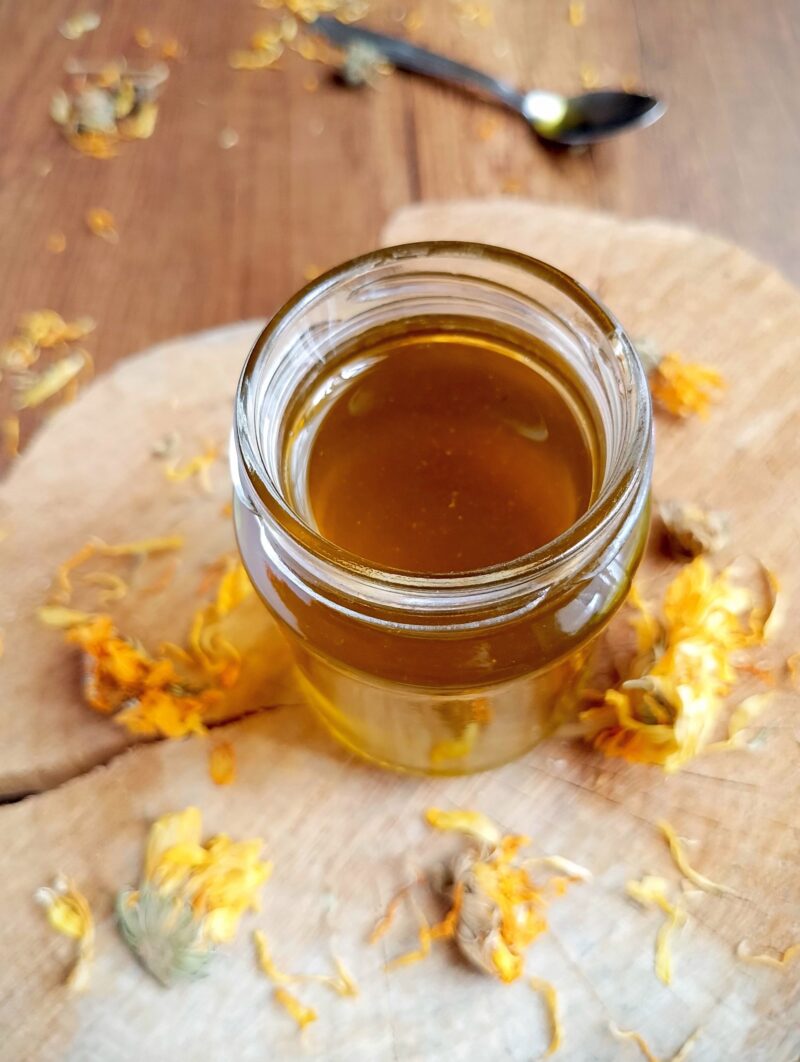 Ready calendula oil in jar with calendula petals scattered around it