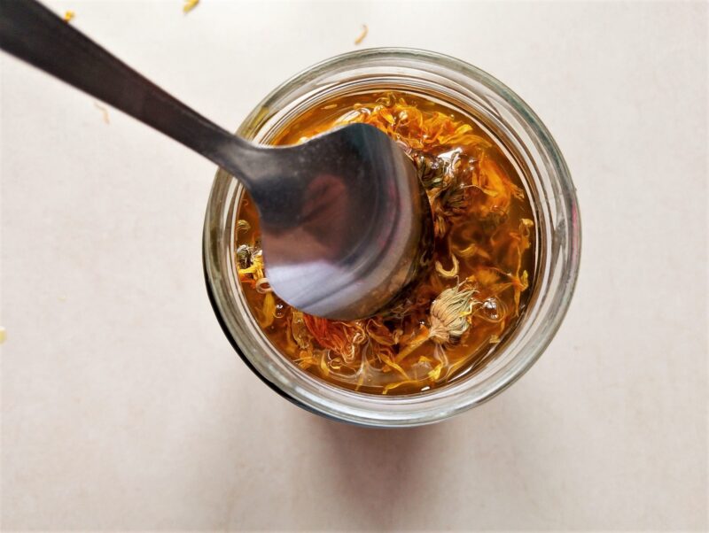 Removing air bubbles from the jar of calendula oil with a spoon