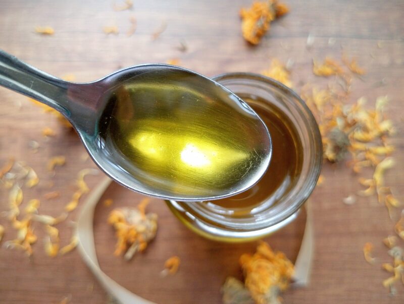 Spoon lifting some of the calendula oil out of the jar