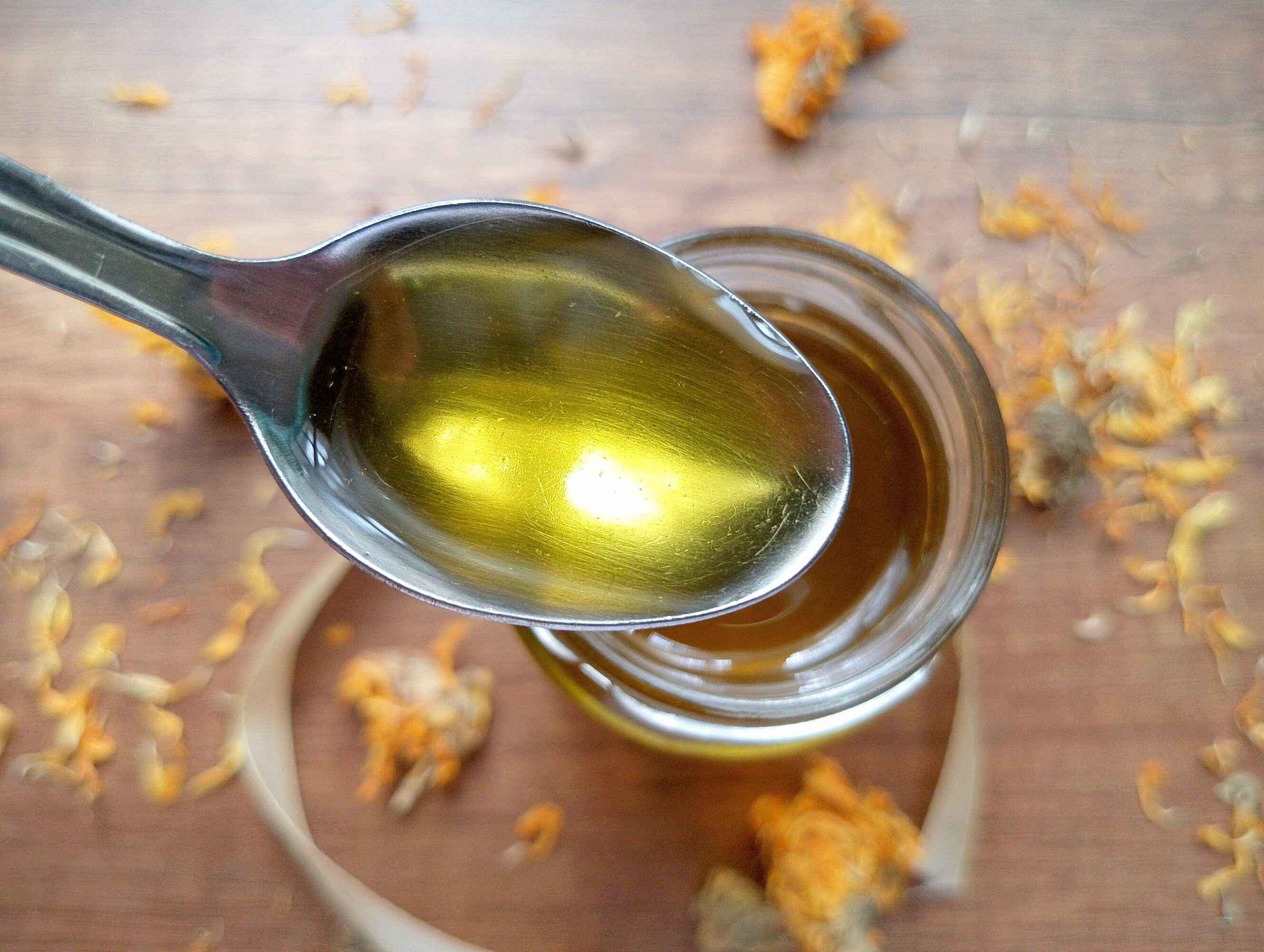 How to make calendula oil: spoon lifting some oil from jar