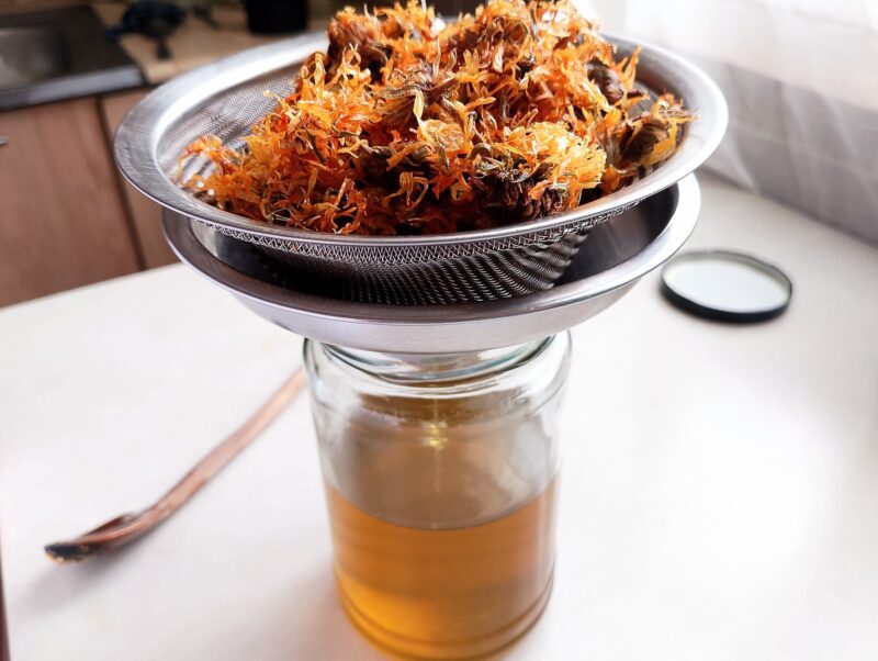 Straining the calendula infused oil on a mesh sieve