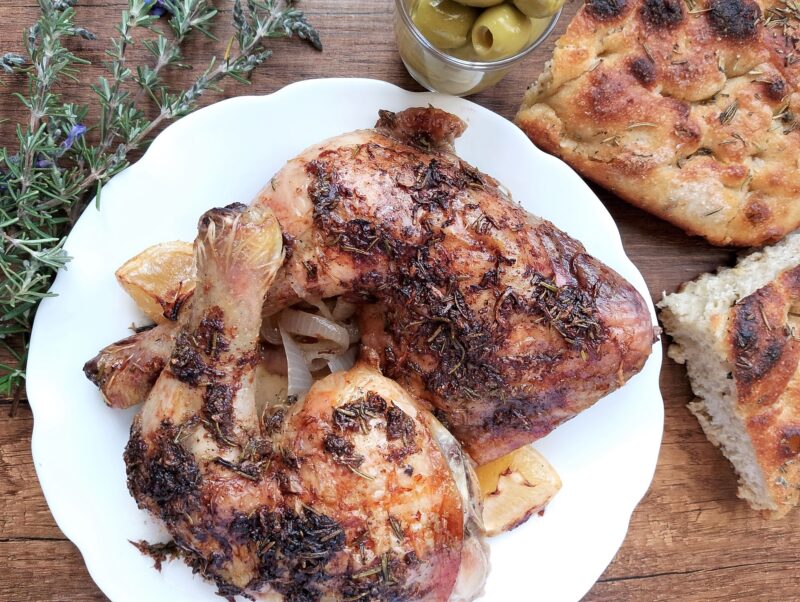 Lemon rosemary chicken quarters on a serving plate with some olives and sourdough focaccia on the side