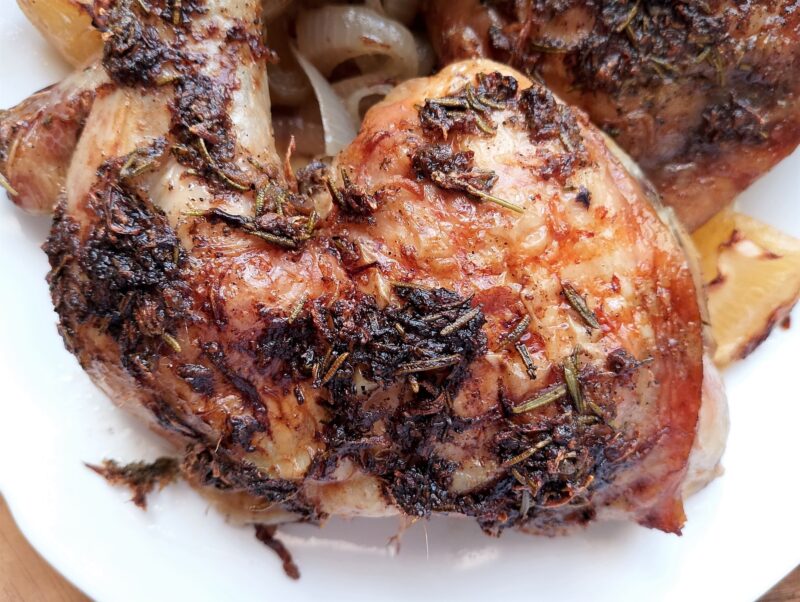 Rosemary lemon roasted chicken leg on a serving platter with lemon wedges and caramelized onion slices