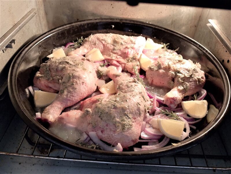 Placing baking pan with rosemary lemon marinated chicken legs in the oven